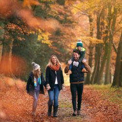 Family Walking Along Autumn Woodland Path With Father Carrying Son On Shoulders