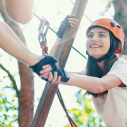 Couple in love man male and woman female adults wear protective helmets and having a date in extreme rope park at green forest. Climbing in rope bridge. Active healthy extreme lifestyle leisure.